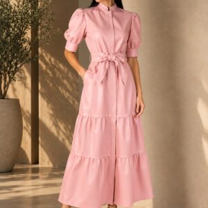 Vestido de couro rosa pastel com mangas bufantes, gola padre, abotoamento frontal, faixa com laço na cintura e saia em camadas